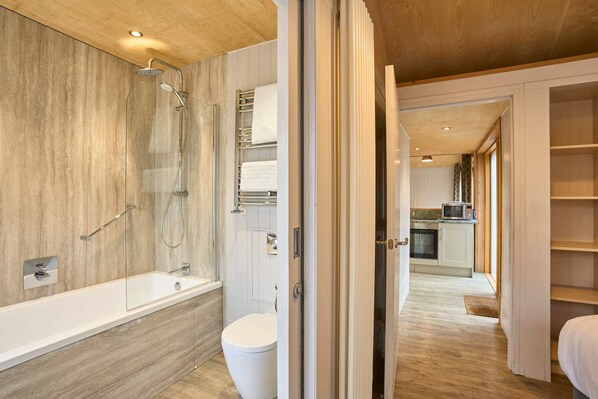 A modern bathroom with a glass-enclosed shower, a white bathtub, and a toilet.