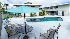 A pool area with a table and chairs, a covered umbrella, and a building in the background.