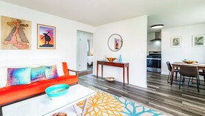 A modern living room with a red sofa, a coffee table, and a patterned rug. There is a dining area with a table and chairs, and a kitchen in the background.
