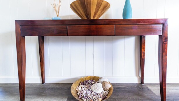 A wooden console table with a decorative bowl below it, against a white paneled wall.