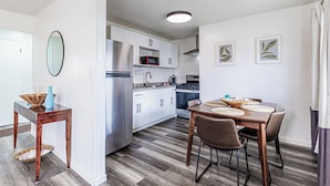 A modern kitchen with white cabinets, stainless steel appliances, and a dining area with a wooden table and chairs.
