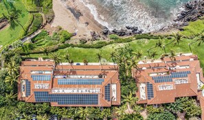 Un resort con varias construcciones que incluyen paneles solares en la azotea, rodeado de abundante vegetación y una playa.