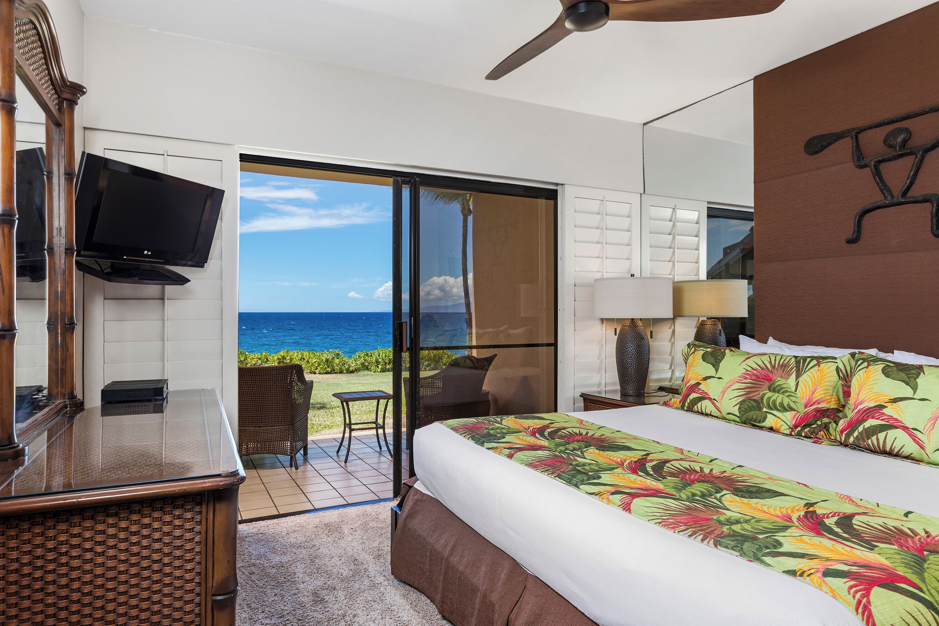 Een hotelkamer met een bed, een televisie, een bureau en uitzicht op de oceaan.