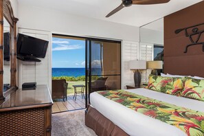 A hotel room with a bed, a television, a desk, and a view of the ocean.