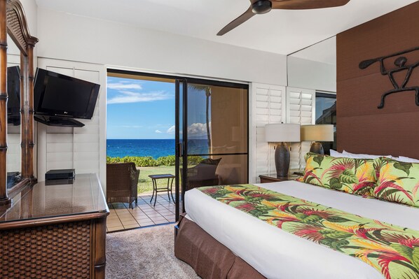 A hotel room with a bed, a television, a desk, and a view of the ocean.