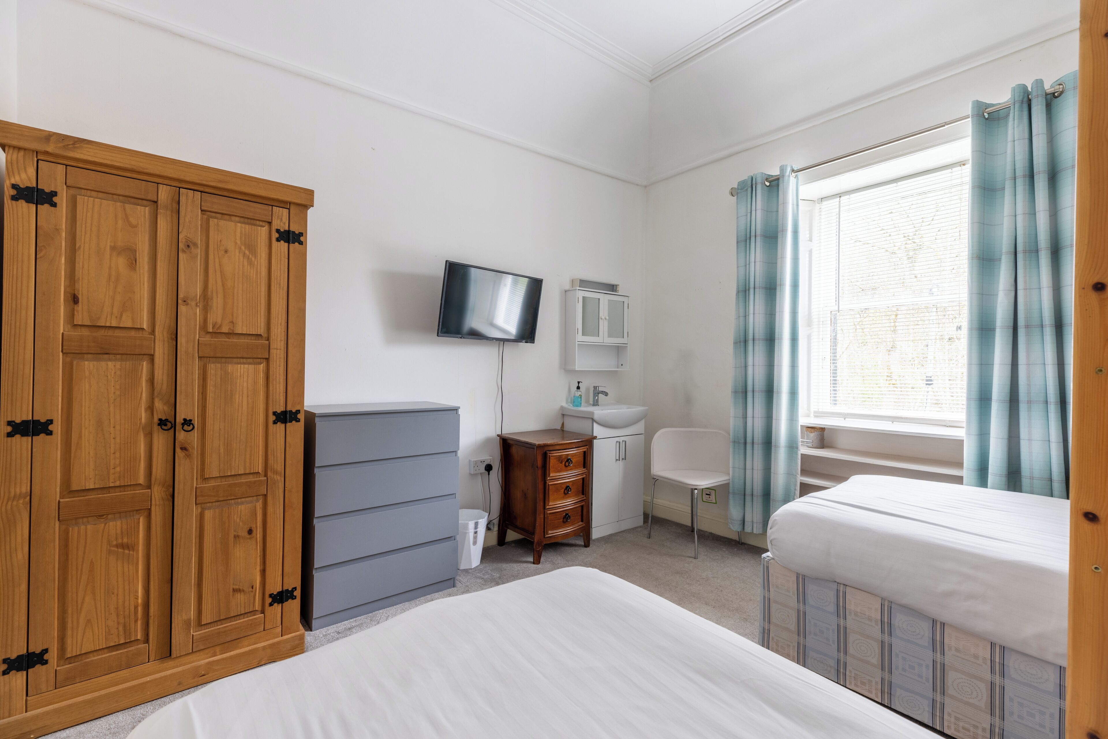 A bedroom with a bed, a wardrobe, a television, a sink, and a window with curtains.