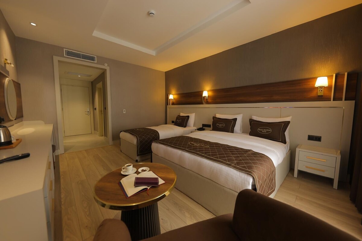 Quarto de hotel com uma cama grande, mesas de cabeceira, uma mesa de centro redonda e uma área de estar com uma poltrona.