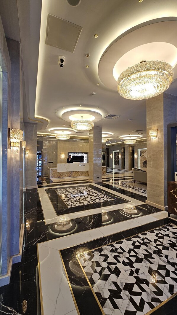 Un vestíbulo amplio con mostrador de recepción, candelabros y piso con diseño.