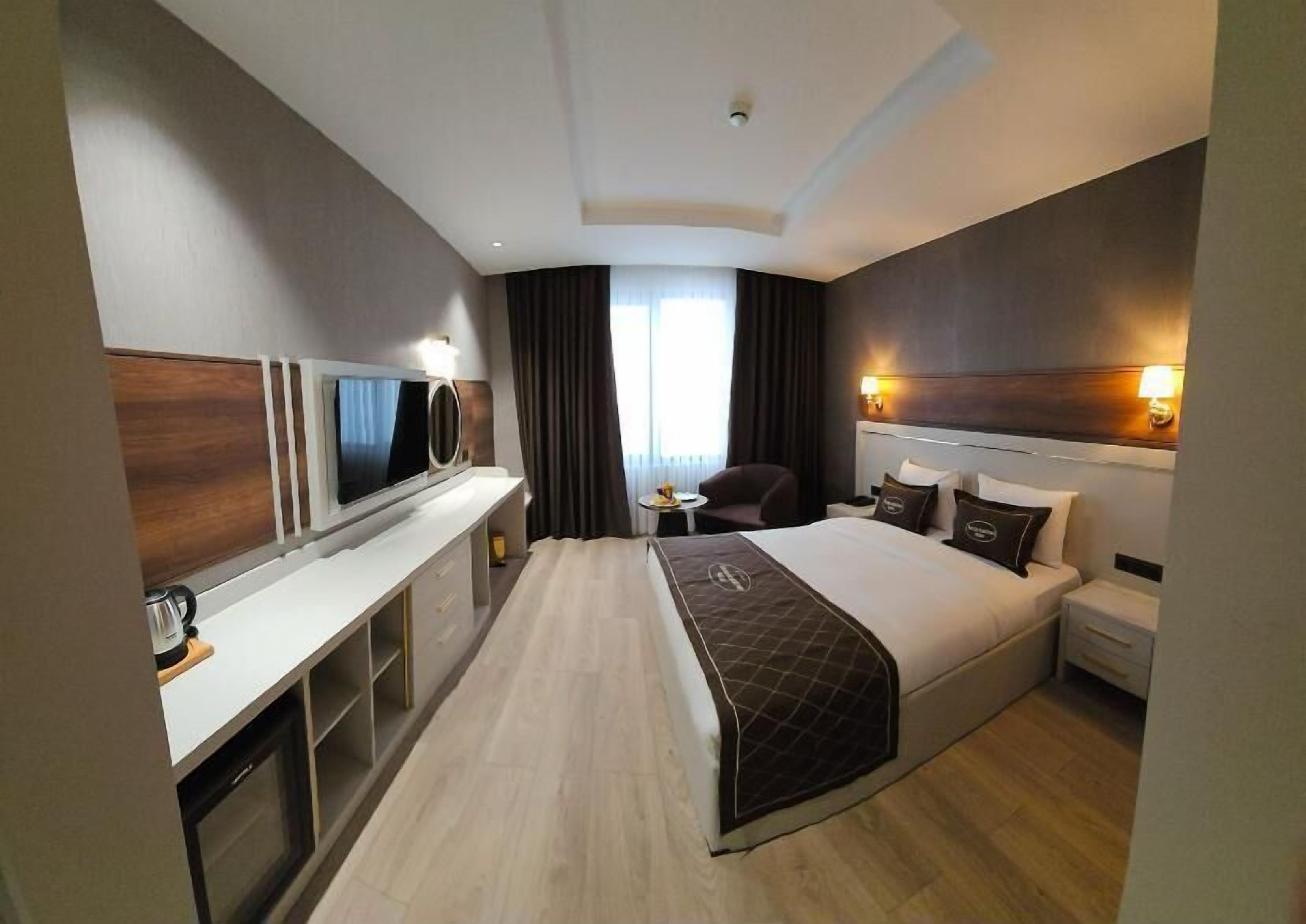 A hotel room with a large bed, a desk with a flat-screen TV, a coffee maker, and a small side table.