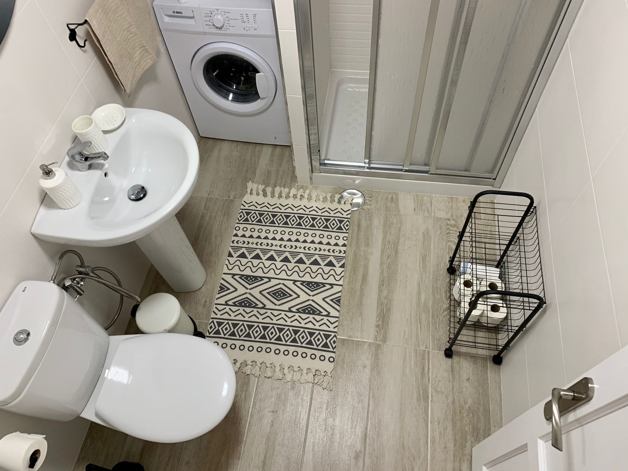A compact bathroom with a washing machine, sink, toilet, and shower area.