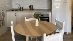 Une cuisine moderne avec des armoires blanches, une hotte de cuisinière en acier inoxydable, un réfrigérateur encastré et une table ronde en bois, accompagnée de chaises.