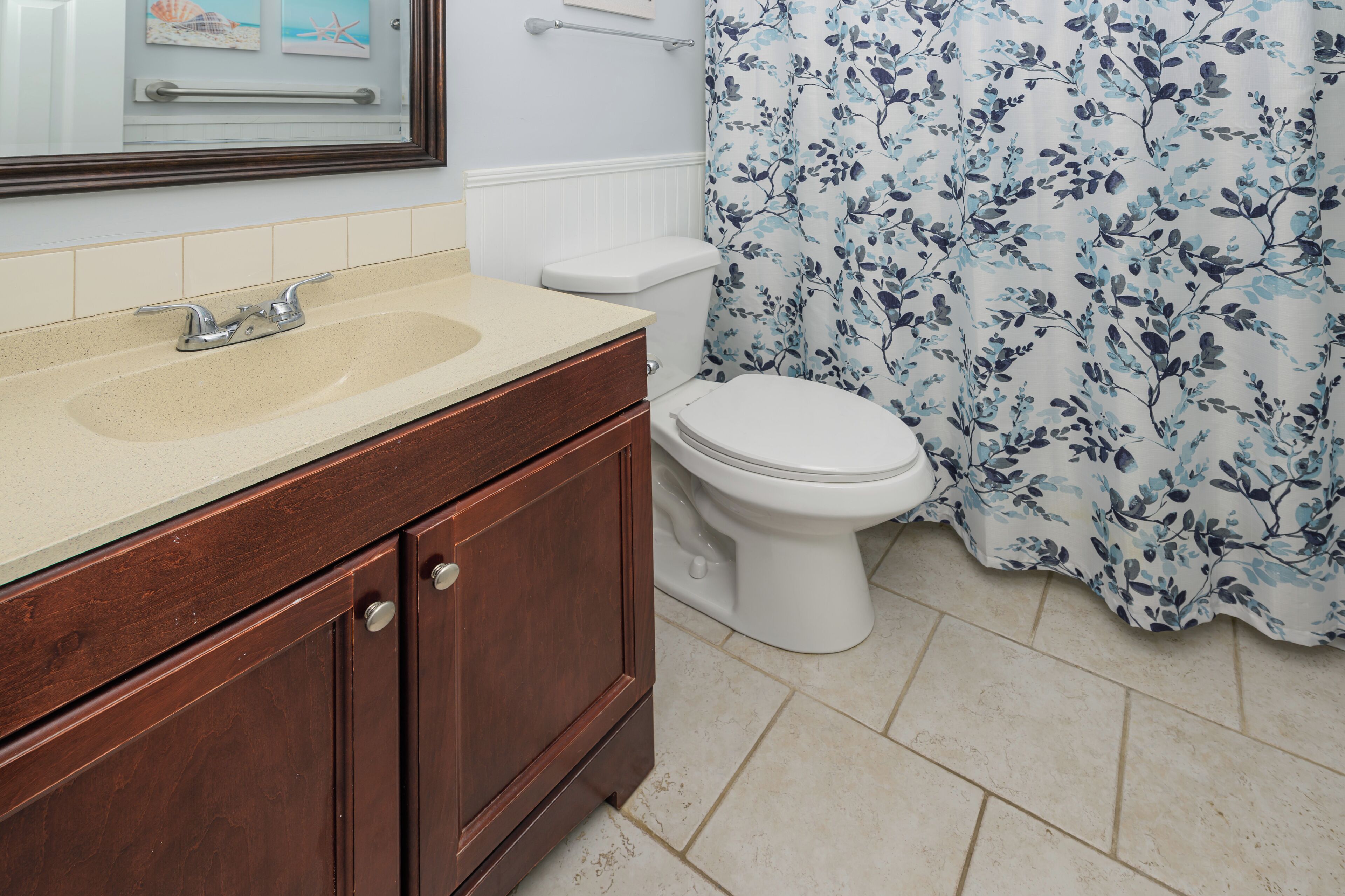 Une salle de bain avec un meuble-lavabo en bois, des toilettes blanches et un rideau de douche à motifs floraux.