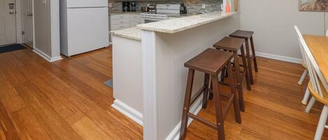 A kitchen with white cabinets, a double oven, a microwave, and a refrigerator. There are wooden stools and a wooden table.