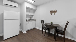 Une cuisine compacte avec des meubles blancs, un réfrigérateur encastré et un coin repas comprenant une table et des chaises en bois foncé.