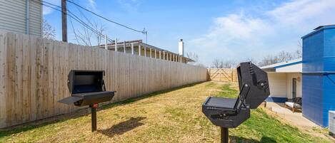A backyard with a wooden fence, a barbecue grill, and a blue utility shed.