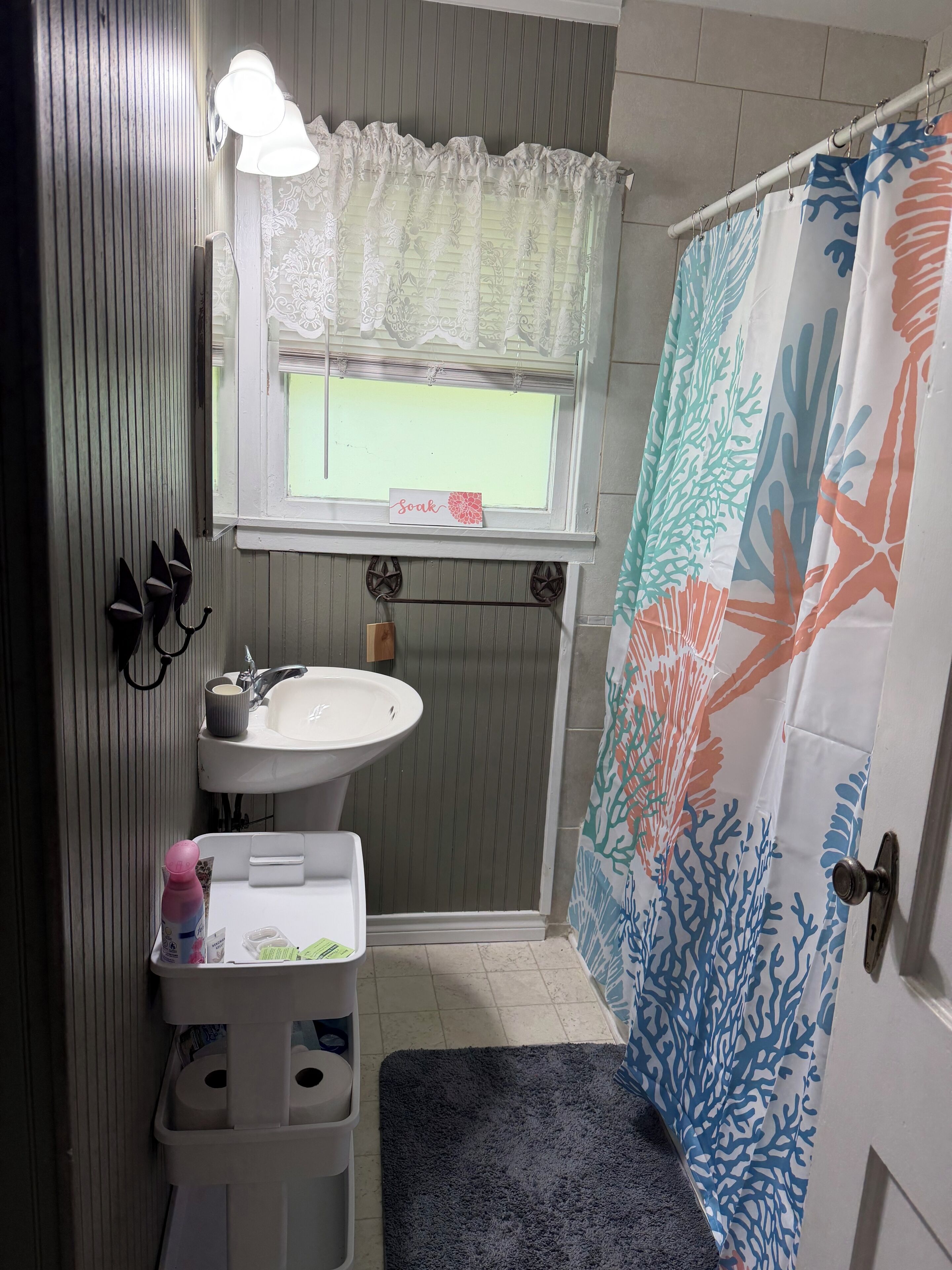 Une salle de bain équipée d’un lavabo, d’un miroir, d’un porte-serviettes et d’un rideau de douche orné d’un motif corallien.