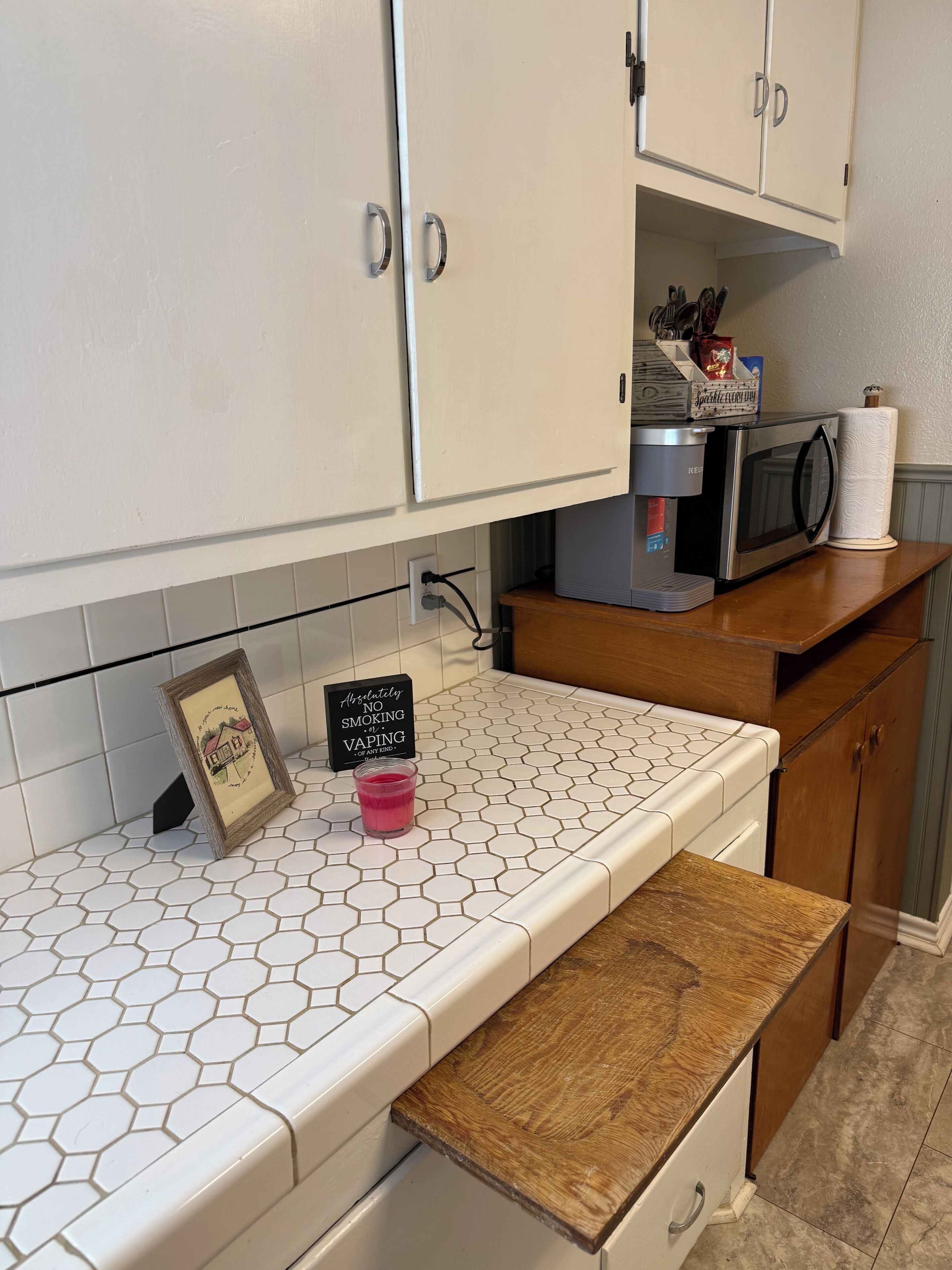 Une cuisine avec des meubles blancs, un four à micro-ondes, un grille-pain et une machine à café posés sur le plan de travail.