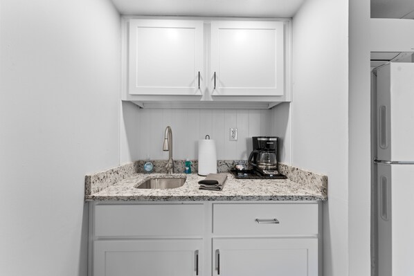 A compact kitchen with white cabinets, a granite countertop, a stainless steel sink, a coffee maker, and a refrigerator. - Sc8- Silver Cove 8 1 Bedroom Condo (Branson)