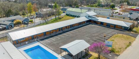 A motel with a swimming pool, a parking lot, and a view of the surrounding area.