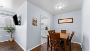 A dining area with a wooden table and chairs, a television mounted on the wall, and a kitchen sign. - Sc3- Silver Cove 3 3 Bedroom Condo (Branson)