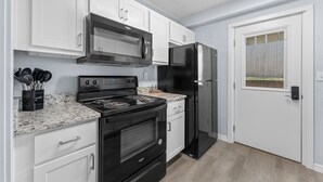 A modern kitchen with white cabinets, a stainless steel microwave, a black refrigerator, and a granite countertop. - Sc3- Silver Cove 3 3 Bedroom Condo (Branson)