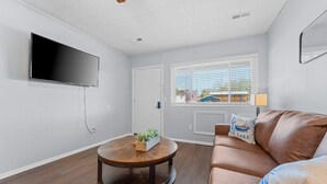 A living room with a flat-screen TV mounted on the wall, a round wooden coffee table with a plant, a brown leather sofa with decorative pillows, and a window with blinds. - Sc2- Silver Cove 2 2 Bedroom Condo (Branson)