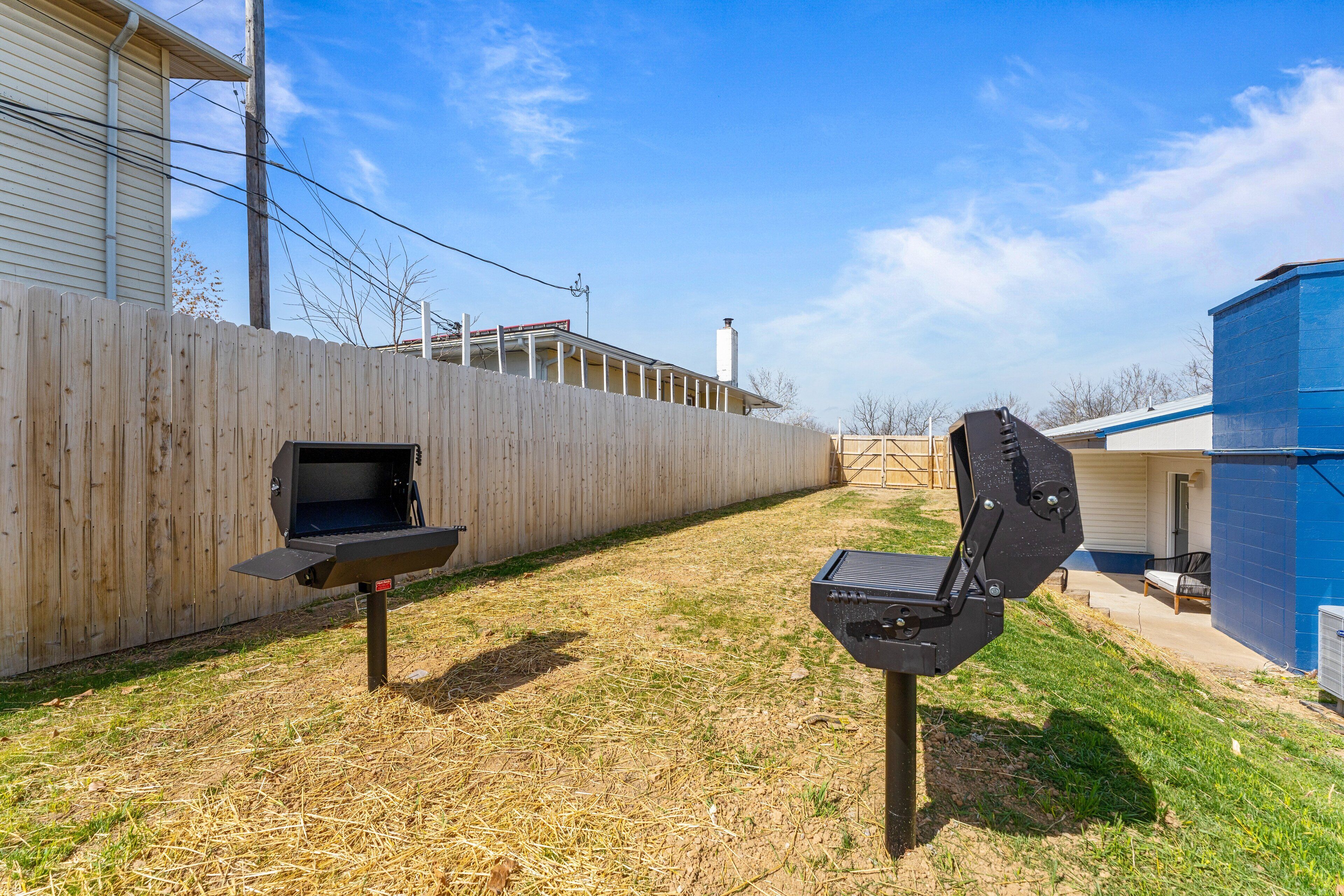 A backyard with a wooden fence, a barbecue grill, and a blue utility shed.