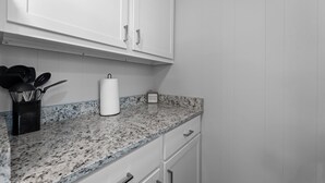 Una cocina con armarios blancos, encimera de granito y cafetera.