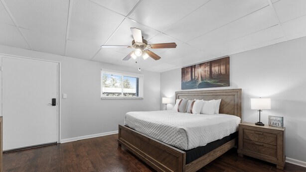 A bedroom with a wooden bed, a ceiling fan, a nightstand with a lamp, and a painting on the wall. - Sc13- Silver Cove 13 1 Bedroom Condo (Branson)