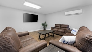 A living room with brown leather sofas, a wooden coffee table, a flat-screen TV mounted on the wall, and an air conditioning unit. - Sc13- Silver Cove 13 1 Bedroom Condo (Branson)