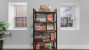 A bookshelf with various board games, including Monopoly and Candy Land, in a room with two windows and a plant. - Sc13- Silver Cove 13 1 Bedroom Condo (Branson)