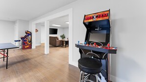 Una habitación con mesa de ping pong, máquina de baloncesto recreativa y taburete de bar.