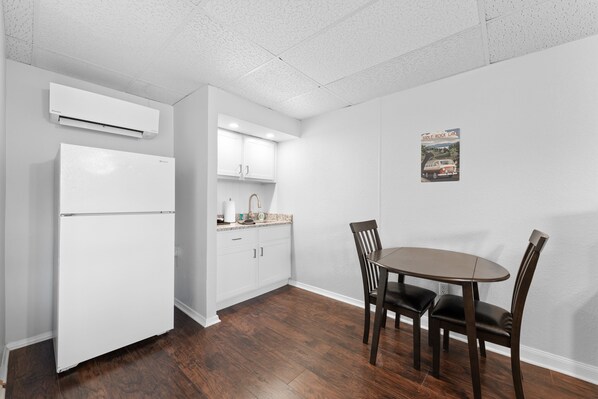 A compact kitchen with white cabinets, a white refrigerator, and a dining area with a wooden table and chairs.
