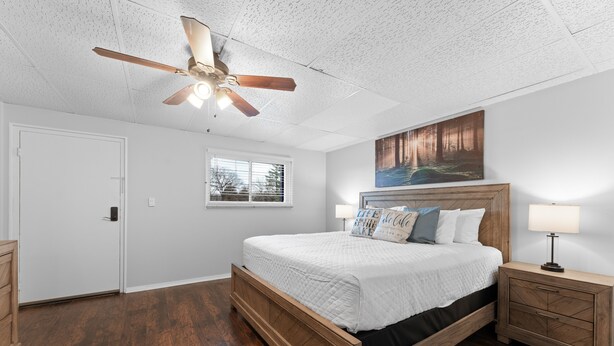 Une chambre avec un lit en bois, un ventilateur de plafond, une fenêtre et un tableau au mur.