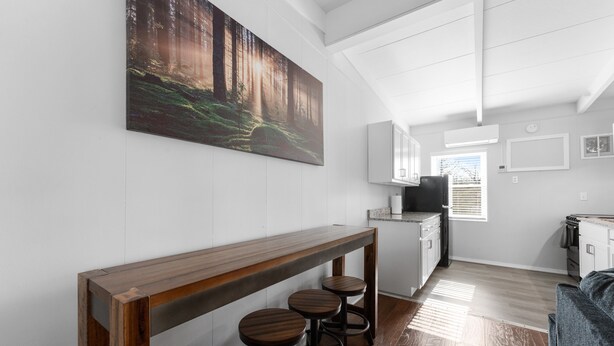 Una cocina moderna con armarios blancos, una barra de bar con taburetes y un cuadro grande con motivos forestales en la pared.