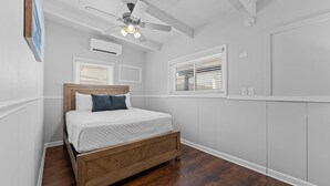 Un dormitorio con cama de madera, paredes blancas, ventilador de techo y ventana con persianas.