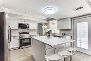 Een moderne keuken met witte kasten, roestvrijstalen apparatuur en een centraal eiland met barstoelen.