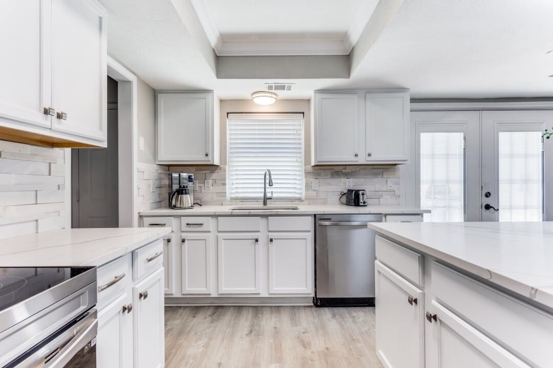 A modern kitchen with white cabinetry, a stainless steel dishwasher, and a built-in oven.