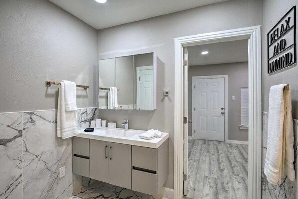 Un baño con salpicadero de mármol, un lavabo blanco y un espejo. Hay un cartel en la pared que dice "RELAX AND UNWIND".