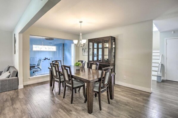 A dining area with a wooden table and chairs, a chandelier, and a view of a blue room through a glass wall.