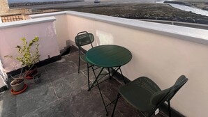 A balcony with a green table and chairs, potted plants, and a view of a beach and distant hills. - Natterjack Cottage - Access to the Western Lakes (Millom)