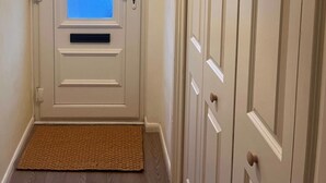 A hallway with a door featuring a frosted glass window, a white doorbell, and a doormat. - Natterjack Cottage - Access to the Western Lakes (Millom)