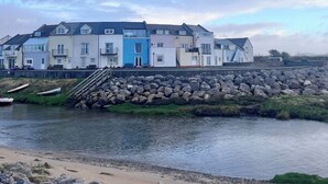 A row of coastal buildings with a stone wall and a sandy beach in the foreground. - Natterjack Cottage - Access to the Western Lakes (Millom)