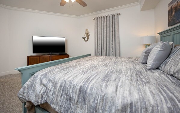 Un dormitorio con una cama, un televisor sobre un mueble de madera, una lámpara de pared y una cortina.