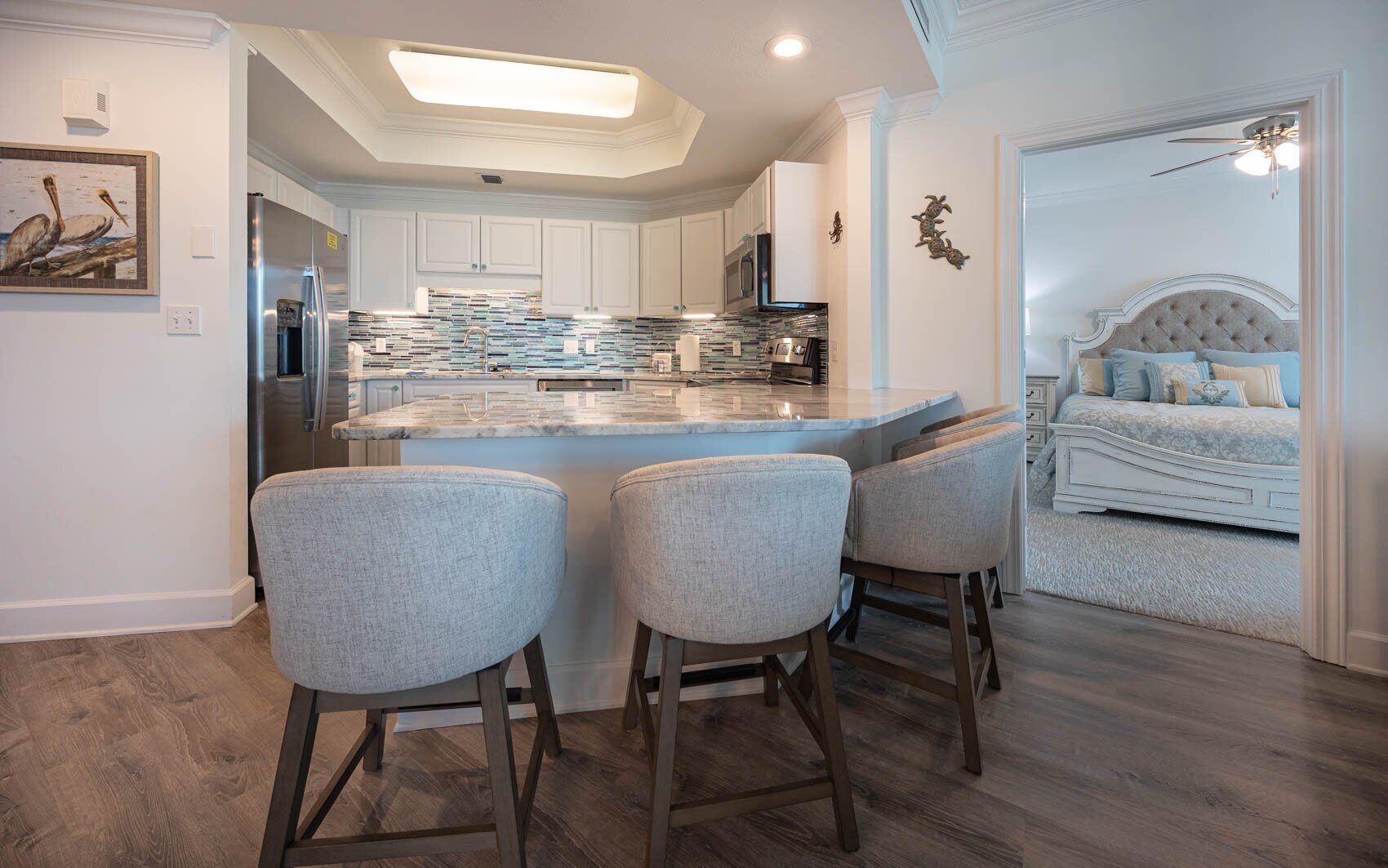 A modern kitchen with a central island, bar stools, and a dining area with a sofa and a bed.