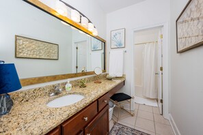 Une salle de bain avec un comptoir en granit, un lavabo, un grand miroir, un porte-serviettes et un rideau de douche.