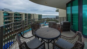 A balcony with wicker furniture and a view of a swimming pool and buildings. - Phoenix On The Bay 1513 3 Bedroom Condo (Orange Beach)