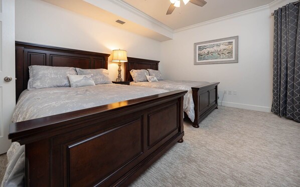 A bedroom with two beds, a ceiling fan, a lamp, a framed picture, and a window with curtains. - Phoenix On The Bay 1513 3 Bedroom Condo (Orange Beach)