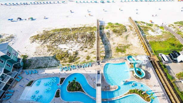 An aerial view of a beach resort with a swimming pool, beach chairs, and a boardwalk.