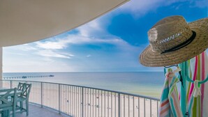 A balcony with a view of the beach and ocean, a straw hat, and striped towels.